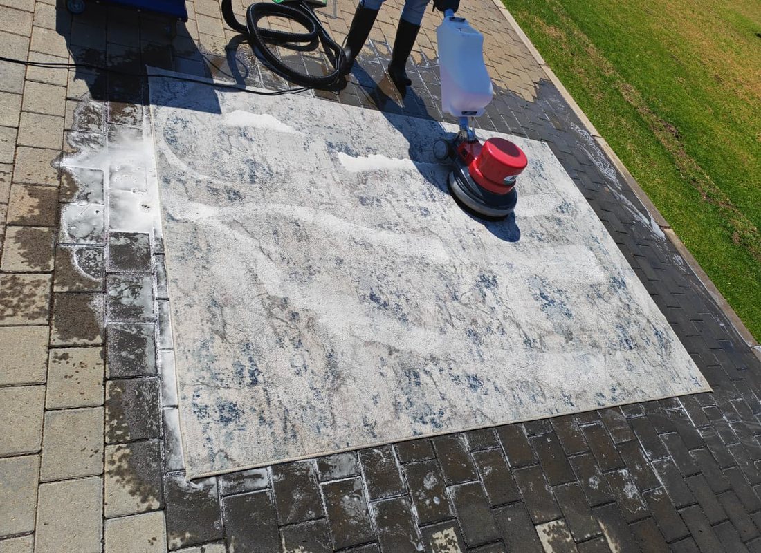 MooiMop cleaning a large rug with an industrial rotary machine on a paved driveway